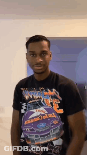 A Young Man Wearing A Black T-Shirt With A Purple Race Car On It Is Standing In A Room . GIF