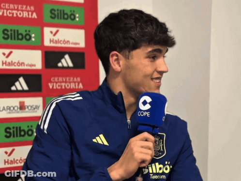 A Young Man Wearing A Blue Adidas Jacket Is Talking Into A Cope Microphone GIF