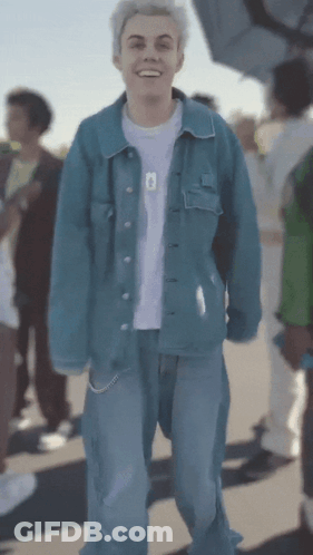 A Young Man Wearing A Blue Denim Jacket And Blue Jeans Is Smiling GIF