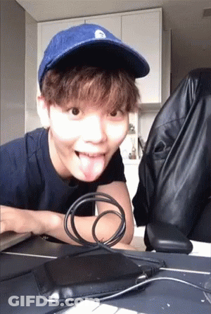 A Young Man Wearing A Blue Hat Is Sticking His Tongue Out While Sitting At A Desk . GIF