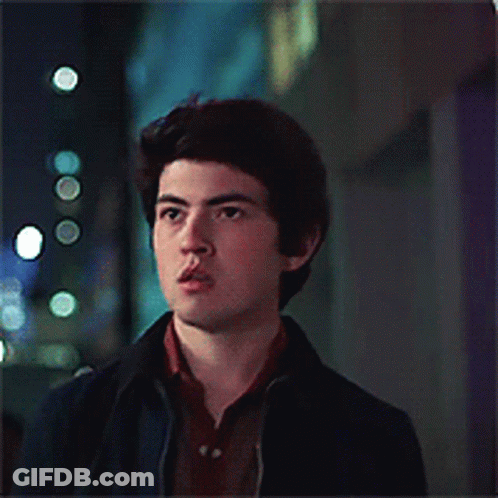 A Young Man Wearing A Blue Jacket And A Brown Shirt Looks At The Camera GIF