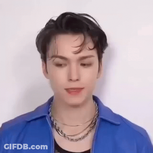 A Young Man Wearing A Blue Jacket And A Necklace Is Looking Down . GIF