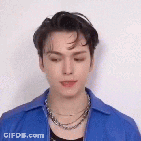 A Young Man Wearing A Blue Jacket And A Necklace Is Making A Funny Face . GIF