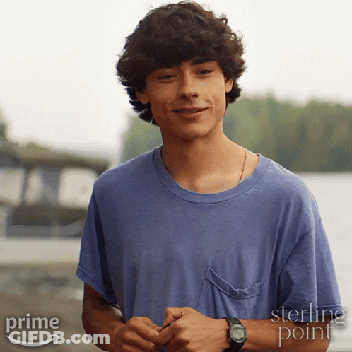 A Young Man Wearing A Blue Shirt And A Watch Is Standing In Front Of A Sign That Says Sterling Point GIF