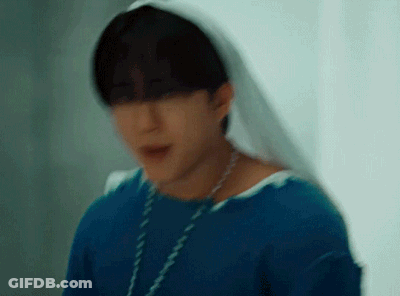 A Young Man Wearing A Blue Shirt And A White Veil Is Standing In Front Of A Window . GIF