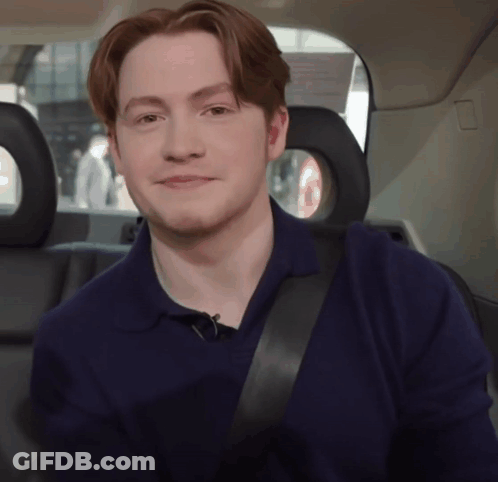 A Young Man Wearing A Blue Shirt And Black Seat Belt Smiles GIF