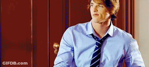 A Young Man Wearing A Blue Shirt And Tie Is Standing In Front Of A Door . GIF