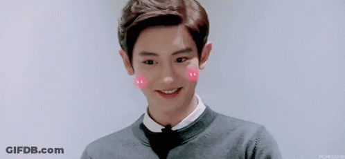 A Young Man Wearing A Bow Tie And A Sweater Is Smiling With Pink Hearts On His Cheeks . GIF