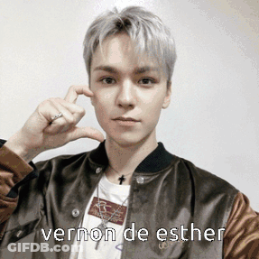 A Young Man Wearing A Brown Jacket Is Making A Heart With His Fingers And The Words Vernon De Esther Below Him GIF