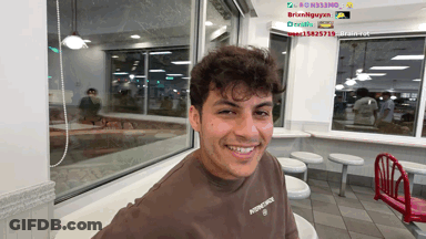 A Young Man Wearing A Brown Shirt That Says Principle Smiles In A Diner GIF
