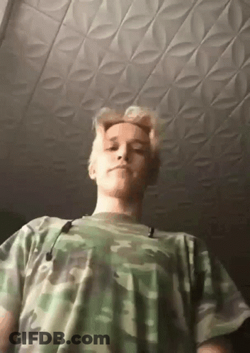A Young Man Wearing A Camouflage Shirt Is Looking Down At The Camera GIF
