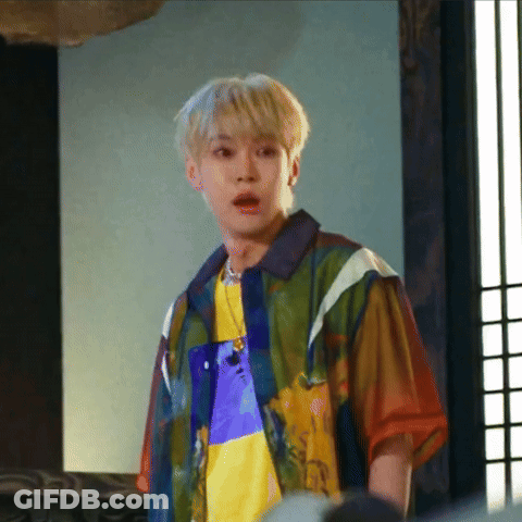 A Young Man Wearing A Colorful Shirt And A Necklace Is Standing In A Room . GIF