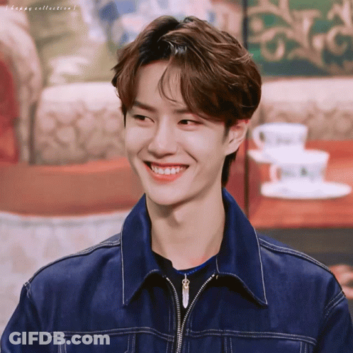 A Young Man Wearing A Denim Jacket Is Smiling In Front Of A Table With Coffee Cups And Saucers GIF