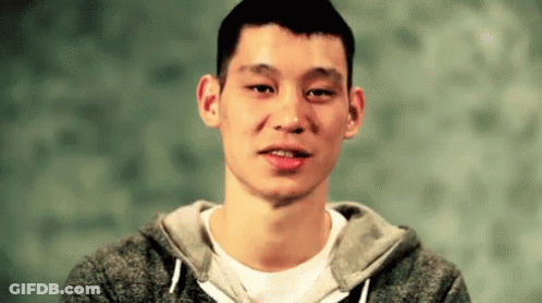 A Young Man Wearing A Gray Hoodie And A White Shirt Is Looking At The Camera . GIF