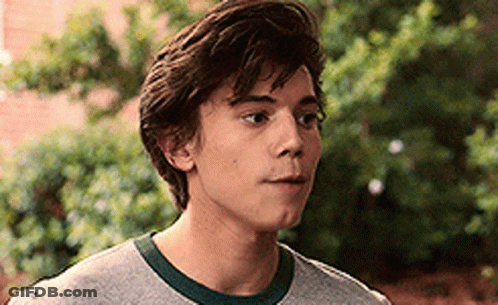 A Young Man Wearing A Gray T-Shirt And A Green Collar Is Looking At The Camera . GIF