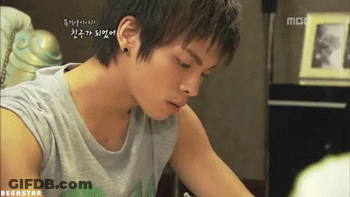 A Young Man Wearing A Gray Tank Top Is Sitting At A Table In Front Of A Mbc TV GIF