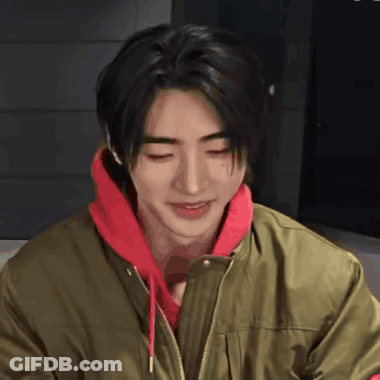 A Young Man Wearing A Green Jacket And A Red Hoodie Smiles GIF