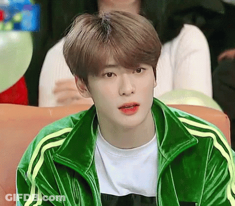 A Young Man Wearing A Green Jacket And White Shirt Is Sitting On A Couch . GIF
