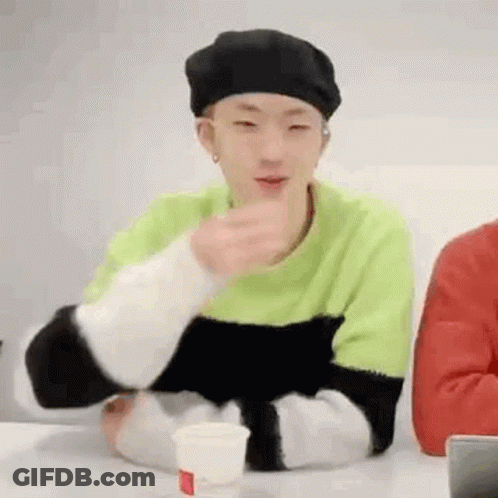 A Young Man Wearing A Green Sweater And A Black Beret Is Sitting At A Table With A Cup Of Coffee . GIF