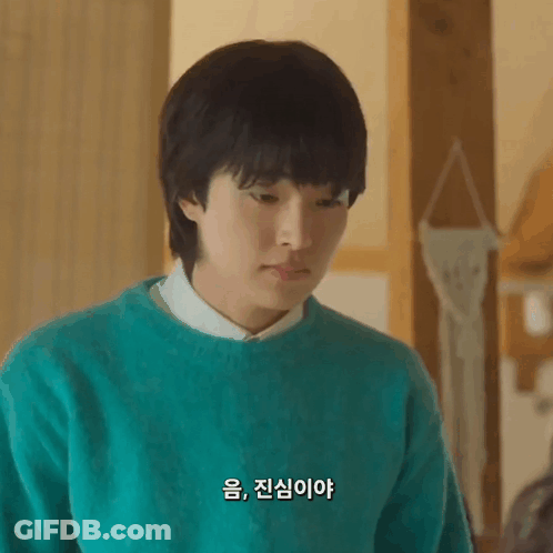 A Young Man Wearing A Green Sweater And A White Shirt Is Looking Down . GIF
