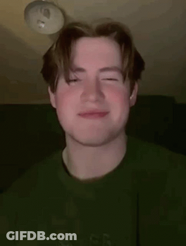 A Young Man Wearing A Green Sweater Is Smiling With His Eyes Closed . GIF