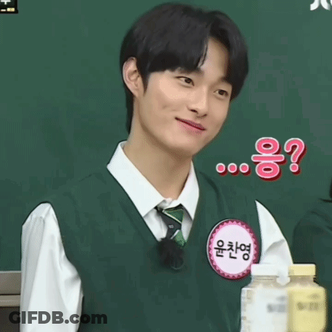 A Young Man Wearing A Green Vest And Tie Is Smiling While Standing In Front Of A Blackboard .. GIF
