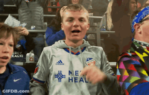 A Young Man Wearing A Grey Adidas Jersey Stands In A Crowd GIF
