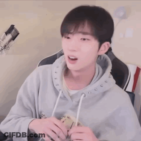 A Young Man Wearing A Grey Hoodie Is Sitting In Front Of A Microphone .. GIF
