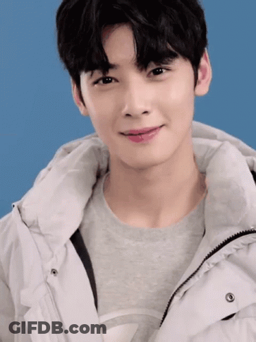 A Young Man Wearing A Grey Shirt And A White Jacket Looks At The Camera GIF