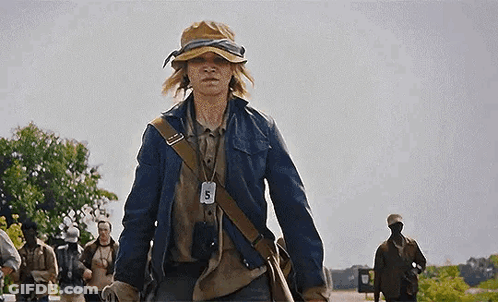 A Young Man Wearing A Hat And A Jacket Is Walking Down A Street . GIF