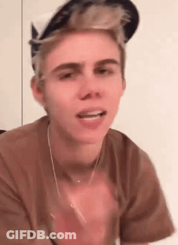 A Young Man Wearing A Hat And A Necklace Is Making A Face . GIF