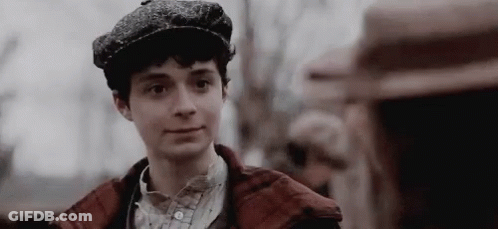 A Young Man Wearing A Hat And A Plaid Jacket Is Smiling . GIF