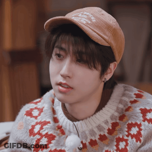A Young Man Wearing A Hat And A Sweater With A Floral Pattern GIF