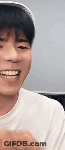 A Young Man Wearing A Hat And A White Shirt Is Smiling And Looking At The Camera . GIF