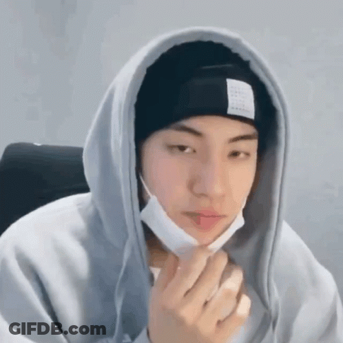 A Young Man Wearing A Hoodie And A Beanie Is Holding His Hand To His Face . GIF