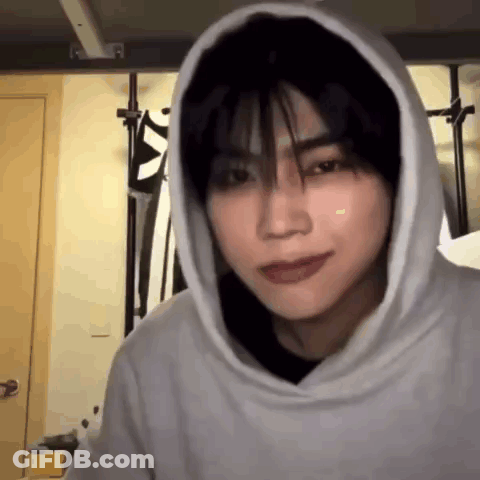A Young Man Wearing A Hoodie Is Looking At The Camera In A Room . GIF