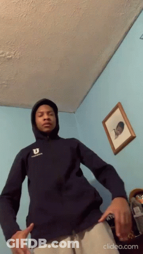 A Young Man Wearing A Hoodie Is Standing In A Room . GIF