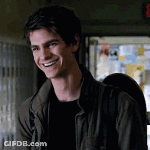 A Young Man Wearing A Jacket And A Backpack Is Smiling In A Room . GIF