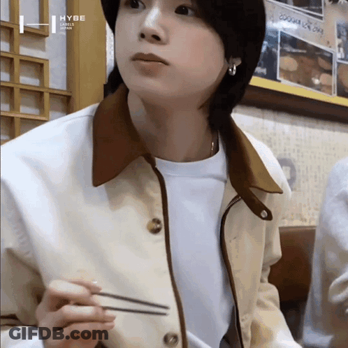 A Young Man Wearing A Jacket And A White Shirt Is Holding Chopsticks In His Hand . GIF