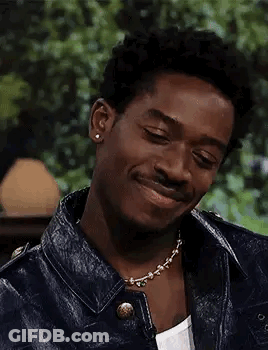 A Young Man Wearing A Leather Jacket And A Necklace Is Smiling . GIF