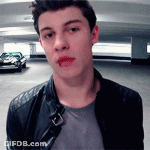 A Young Man Wearing A Leather Jacket Is Standing In A Parking Garage Looking At The Camera . GIF