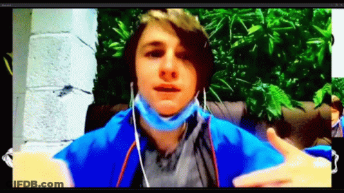 A Young Man Wearing A Mask And Ear Buds Is Sitting In Front Of A Computer Screen . GIF
