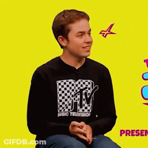 A Young Man Wearing A Mtv Music Television Shirt Is Sitting On A Yellow Background . GIF