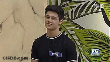 A Young Man Wearing A Name Tag With The Name Rhys On It GIF