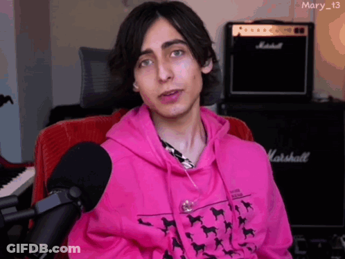 A Young Man Wearing A Pink Hoodie Is Sitting In Front Of A Marshall Amplifier GIF