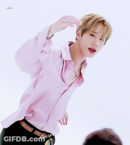 A Young Man Wearing A Pink Shirt And Black Pants Is Standing In Front Of A White Background GIF