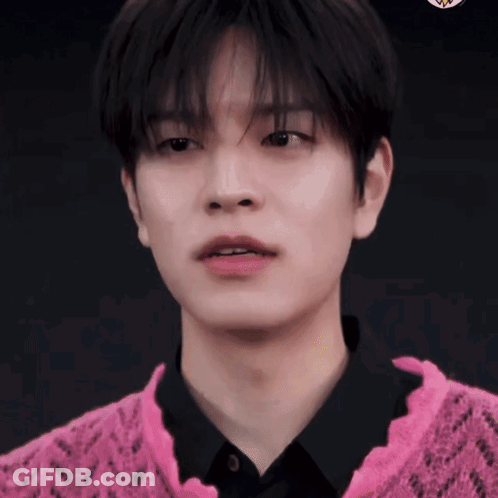 A Young Man Wearing A Pink Sweater And A Black Shirt Is Looking At The Camera . GIF
