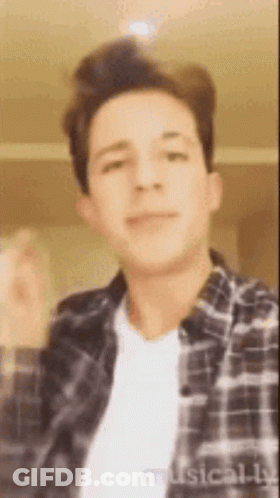 A Young Man Wearing A Plaid Shirt And A White T-Shirt Is Making A Funny Face . GIF