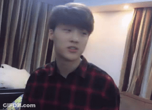 A Young Man Wearing A Plaid Shirt Is Sitting In A Room With Curtains . GIF