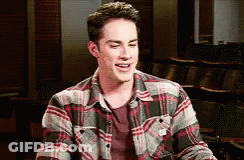 A Young Man Wearing A Plaid Shirt Is Smiling In A Classroom . GIF